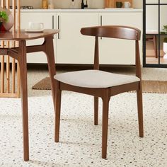 a wooden chair sitting on top of a rug in front of a table and cabinets