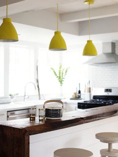 a kitchen with yellow lights hanging from the ceiling and stools in front of an island