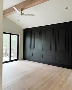 an empty room with black walls and wooden floors, ceiling fan in the center area