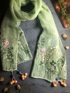 a green scarf with flowers and stones on the ground next to it's edge