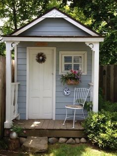 a white chair sitting in front of a small blue house with flowers on the window sill