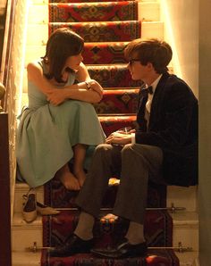 a man and woman sitting on top of a set of stairs next to each other