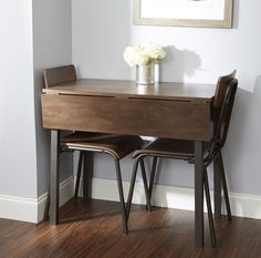 a wooden desk with two chairs next to it and a flower vase on the table