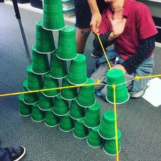 two boys are playing with green cups on the floor in front of a pile of them