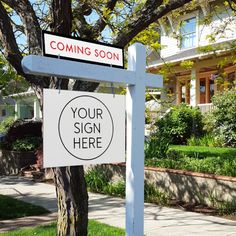 a real estate sign in front of a house with a yard and trees behind it