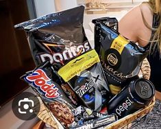 a woman sitting on a couch holding a basket filled with snacks and candy bars in front of her face