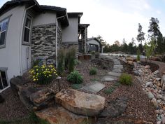 a house that is next to some rocks and flowers in the front yard, with a rock pathway leading up to it