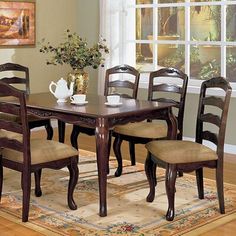 a dining room table with four chairs and a vase on the rug in front of it