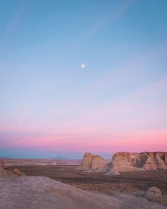 the moon is setting in the sky over some desert land with rocks and sand on it