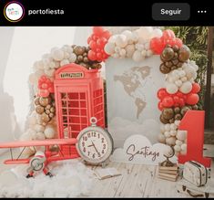 a red phone booth with balloon decorations and a clock on the table next to it