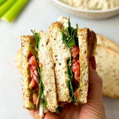 a hand holding a sandwich with tomatoes, lettuce and mayonnaise