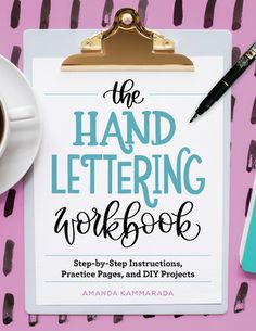 the hand lettering workbook is next to a cup of coffee on a pink surface