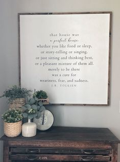 a wooden table topped with a vase filled with flowers next to a framed quote on the wall