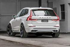 the rear end of a white volvo suv parked in front of a garage with its door open