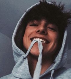 a young man wearing a hoodie and holding a toothbrush in his mouth while smiling