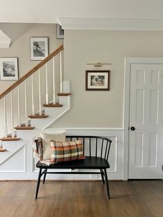 a black bench sitting in front of a stair case next to a white door and some pictures on the wall