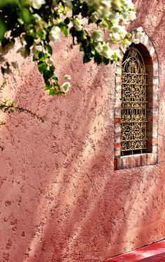 a red bench sitting in front of a pink wall with a window on it's side