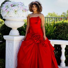 a woman in a red dress standing next to a white vase with flowers on it