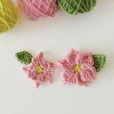 two crocheted flowers are next to balls of yarn