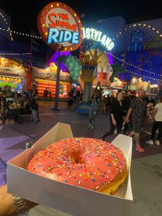 a donut with sprinkles sitting in a box on the ground at an amusement park