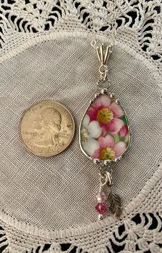 a coin sitting on top of a doily next to a necklace with pink flowers