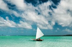 a person on a sailboat in the ocean under a cloudy blue sky with white clouds