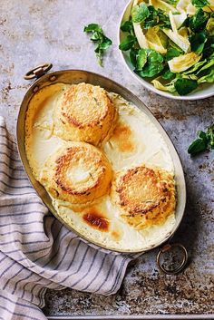 three scallops in a pan next to a bowl of salad on a table