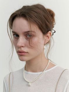 a woman wearing a necklace with pearls on the bottom and a white t - shirt