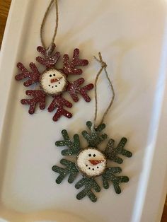 two snowman ornaments are hanging from twine strings on a white tray with brown string