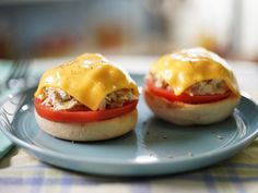 two open faced sandwiches with cheese and tomatoes on a blue plate next to a fork