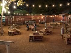 an outdoor seating area with tables and lights strung from the trees in front of it