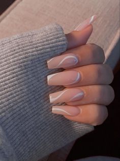 a woman's hand with long, almond colored nails and white swirls on it