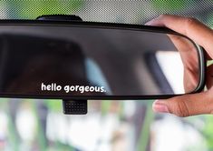 a person holding up a car mirror with the word hello gorgeous written in white on it