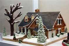 a gingerbread house with snow on the roof and trees around it, in front of a window