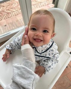 a baby sitting in a high chair with a cast on it's leg and smiling at the camera