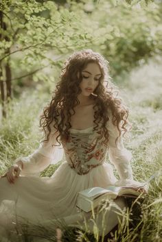 a woman is sitting in the grass with her hair blowing back and eyes closed, reading a book