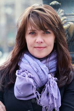 a woman wearing a purple scarf standing in front of a statue and looking at the camera