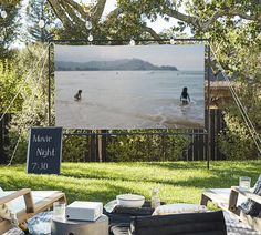 an outdoor movie is set up on the lawn with chairs and tables in front of it