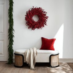 a white bench with a red pillow and wreath on the wall