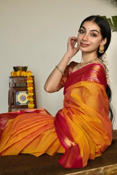 a woman sitting on top of a wooden table wearing a yellow and red sari