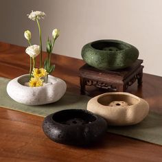 three vases with flowers in them sitting on a wooden table next to a green mat