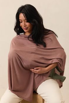 a woman sitting on top of a stool wearing a brown ponchy over her belly