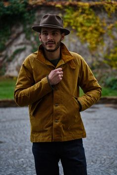 a man wearing a brown hat and jacket standing in the rain with his hands on his hips