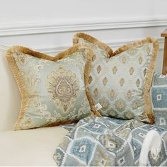 two decorative pillows sitting on top of a bed next to a pillow case and chair