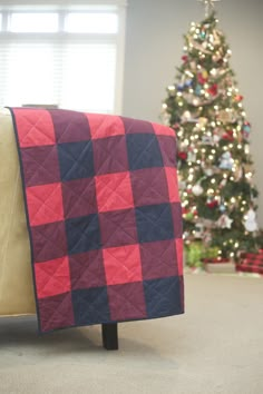 a red and blue blanket sitting on top of a couch next to a christmas tree