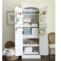 an open cabinet with lots of towels and other items on it in a room that has hardwood floors