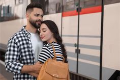 a man and woman standing next to a train with their hands on each other's shoulder