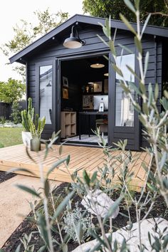 a black shed with an open door and plants in the foreground on a wooden deck