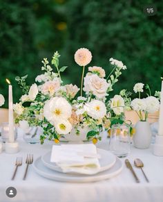 a table set with white and pink flowers, candles and napkins in vases