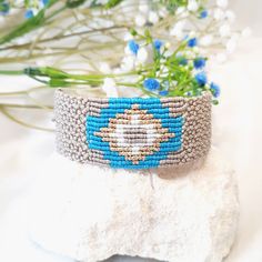 a blue and white beaded bracelet sitting on top of a rock next to flowers